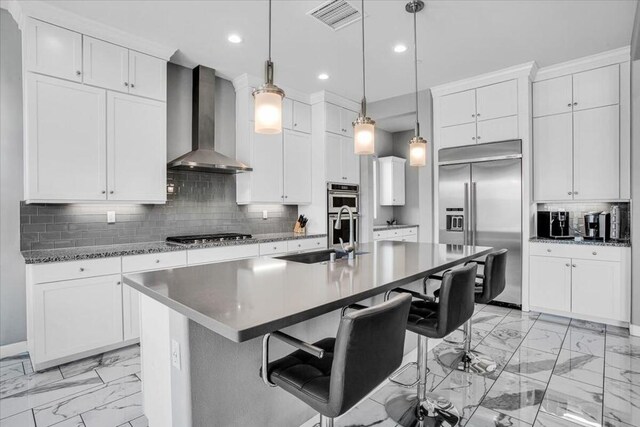 kitchen with a kitchen bar, wall chimney exhaust hood, sink, pendant lighting, and stainless steel appliances