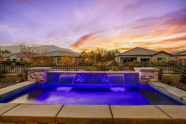 pool at dusk with pool water feature and an in ground hot tub