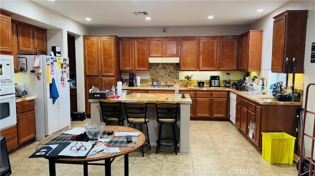 kitchen featuring sink, a kitchen breakfast bar, light tile patterned flooring, white appliances, and a kitchen island