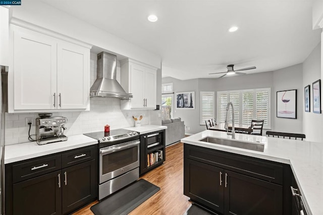 kitchen featuring ceiling fan, electric range, wall chimney exhaust hood, white cabinets, and sink