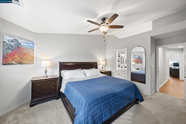 bedroom with ceiling fan, vaulted ceiling, light carpet, and connected bathroom