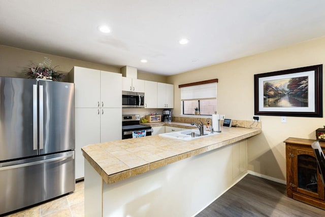 kitchen featuring sink, light hardwood / wood-style flooring, kitchen peninsula, white cabinets, and appliances with stainless steel finishes