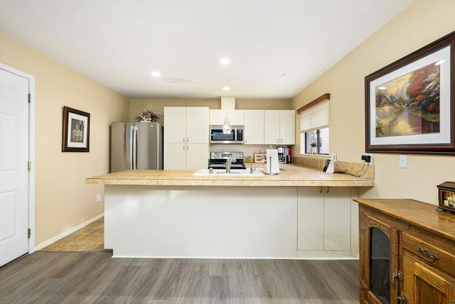 kitchen featuring kitchen peninsula, appliances with stainless steel finishes, sink, white cabinets, and dark hardwood / wood-style floors