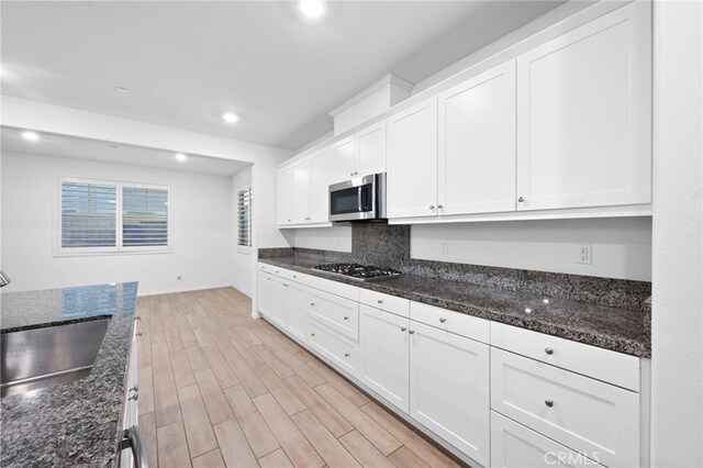 kitchen with sink, light hardwood / wood-style flooring, dark stone countertops, white cabinetry, and stainless steel appliances