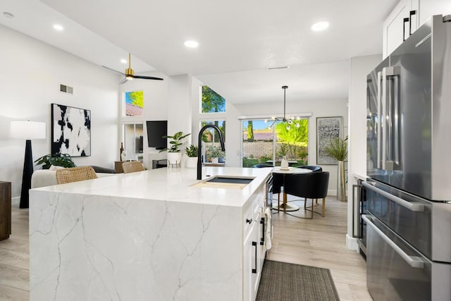 kitchen featuring stainless steel refrigerator, light stone countertops, sink, an island with sink, and white cabinets