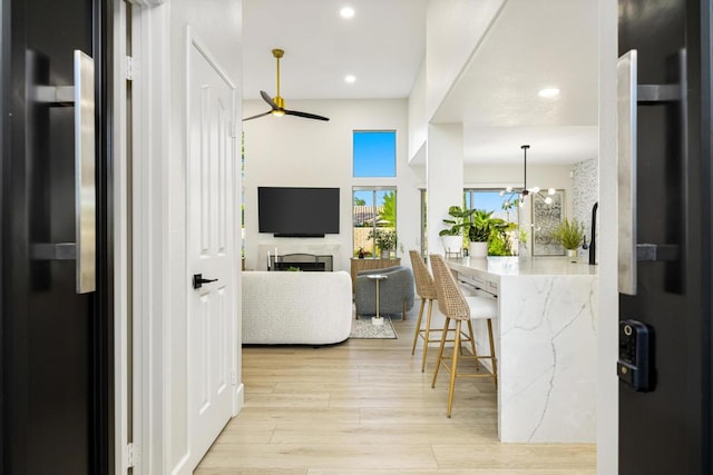 kitchen featuring hanging light fixtures, light hardwood / wood-style flooring, refrigerator, a breakfast bar, and ceiling fan with notable chandelier