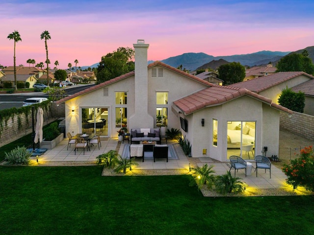 back house at dusk featuring a lawn, outdoor lounge area, a mountain view, and a patio