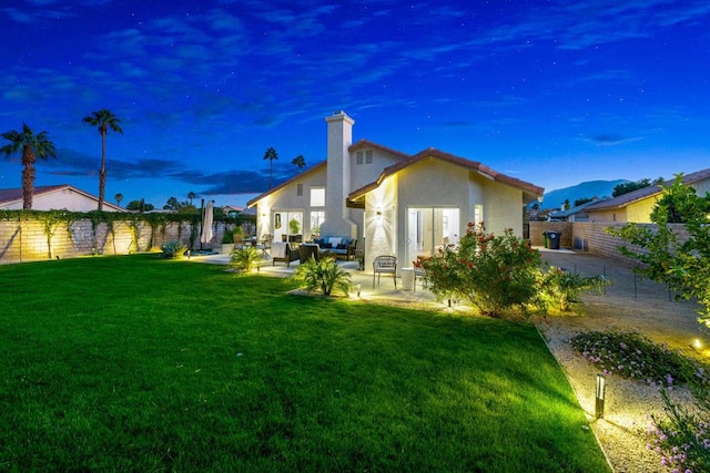 back house at dusk with outdoor lounge area, a yard, and a patio area