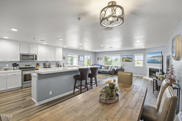 kitchen with a kitchen island, light wood-type flooring, appliances with stainless steel finishes, a kitchen breakfast bar, and white cabinets