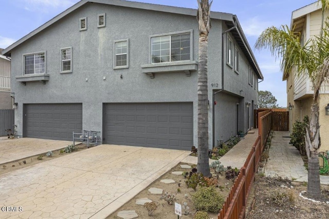 view of front facade with an attached garage, fence, driveway, and stucco siding