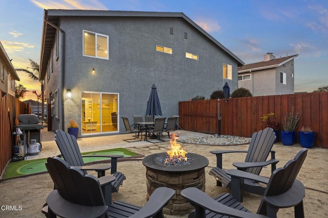 back of house at dusk with a patio, stucco siding, a fenced backyard, and an outdoor fire pit