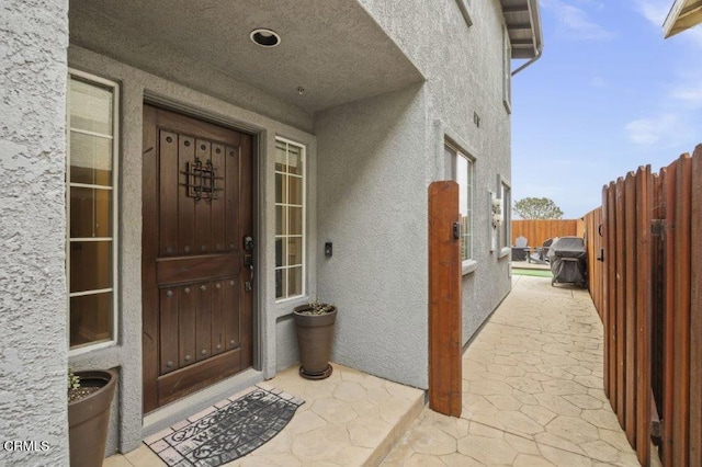 property entrance featuring stucco siding, a patio area, and fence