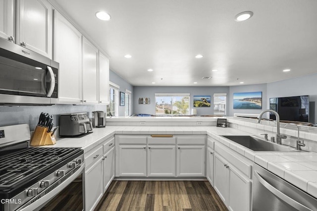 kitchen with a sink, tile countertops, appliances with stainless steel finishes, white cabinets, and dark wood-style flooring