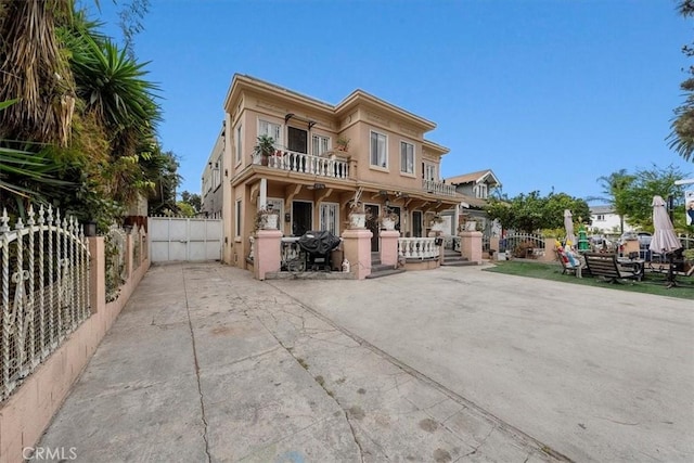 view of front of home featuring a balcony, a gate, fence, and stucco siding