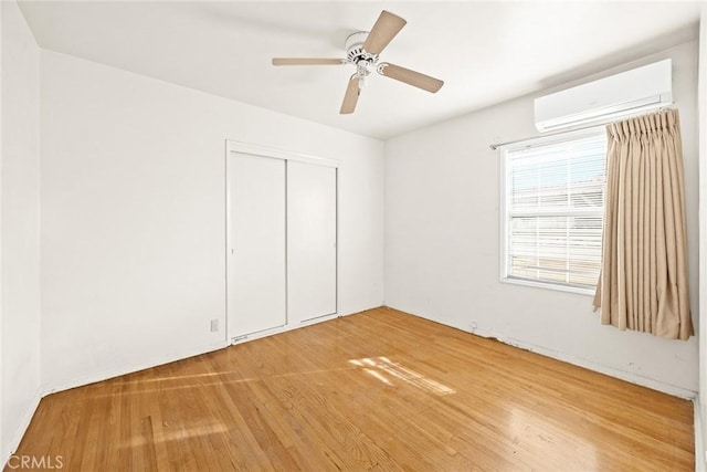 unfurnished bedroom featuring a wall mounted air conditioner, wood-type flooring, a closet, and ceiling fan