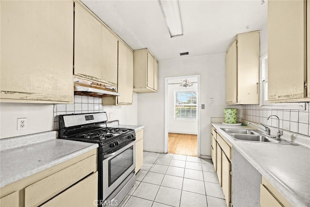 kitchen with cream cabinetry, light tile patterned floors, gas stove, and sink