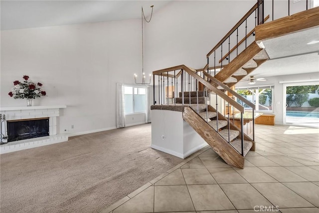 stairway featuring a fireplace, carpet floors, high vaulted ceiling, and ceiling fan with notable chandelier