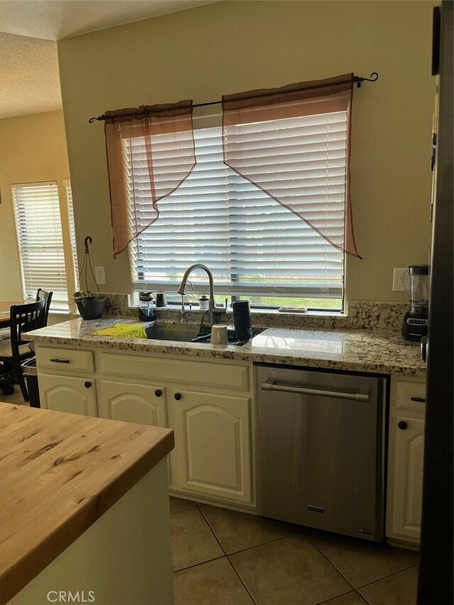 kitchen with dishwasher, light stone counters, white cabinetry, and light tile patterned floors