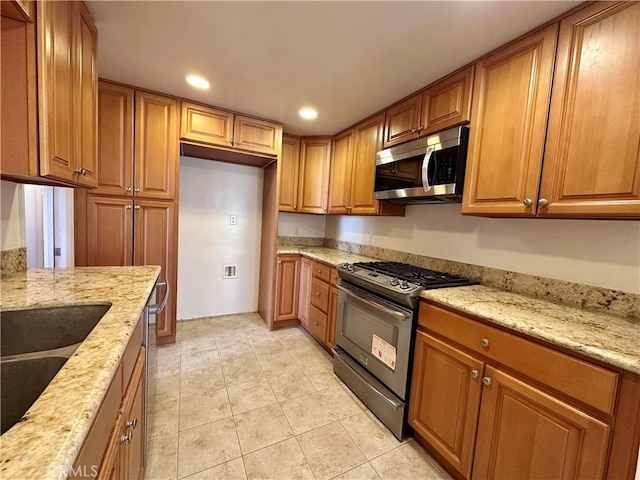 kitchen featuring stainless steel appliances, light stone countertops, sink, and light tile patterned floors