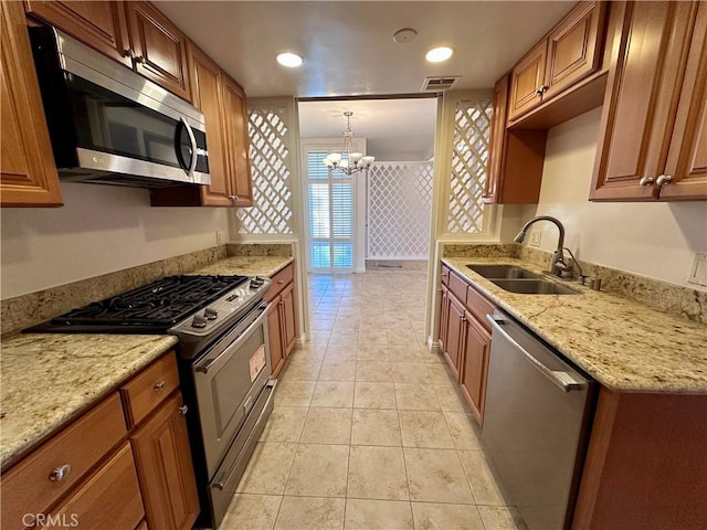 kitchen with sink, appliances with stainless steel finishes, light stone countertops, light tile patterned flooring, and decorative light fixtures