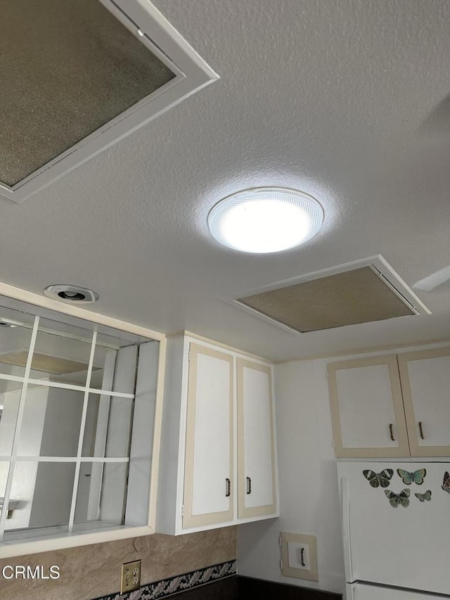 room details with white cabinets, white fridge, and a textured ceiling