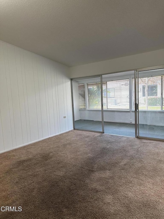 carpeted spare room featuring wood walls and a textured ceiling