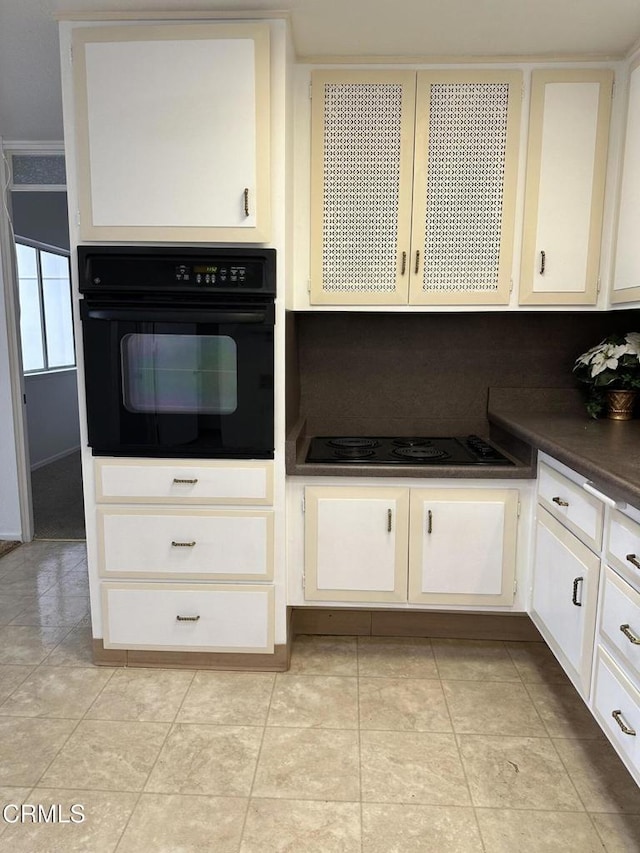 kitchen featuring white cabinets, light tile patterned floors, stovetop, and black oven