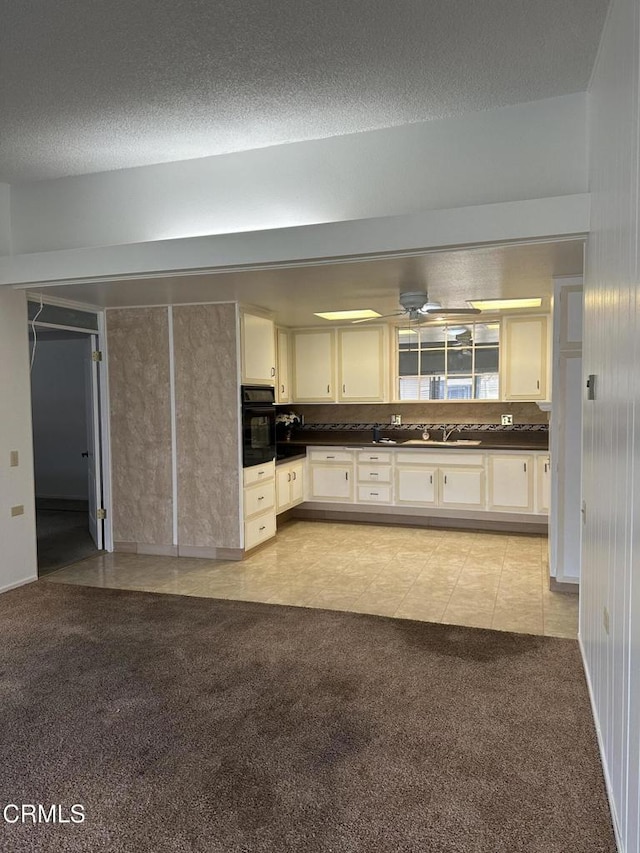 kitchen featuring light carpet, a textured ceiling, ceiling fan, sink, and oven