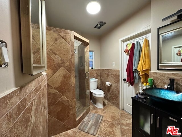 bathroom with a shower with door, vanity, tile walls, and toilet