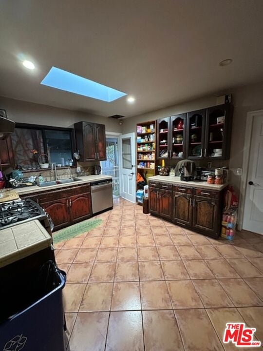 kitchen with a skylight, sink, stainless steel dishwasher, dark brown cabinets, and range