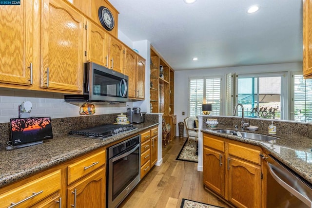 kitchen with appliances with stainless steel finishes, tasteful backsplash, dark stone counters, sink, and light hardwood / wood-style floors