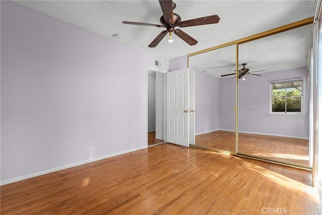 unfurnished bedroom with ceiling fan, hardwood / wood-style floors, a closet, and a textured ceiling