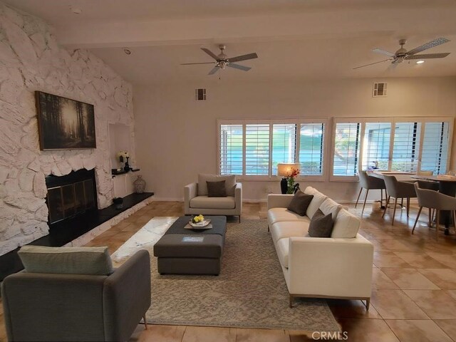 living room with beam ceiling, light tile patterned floors, ceiling fan, and a stone fireplace