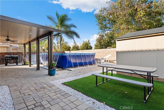 view of yard featuring a fenced in pool, a patio area, ceiling fan, and a shed