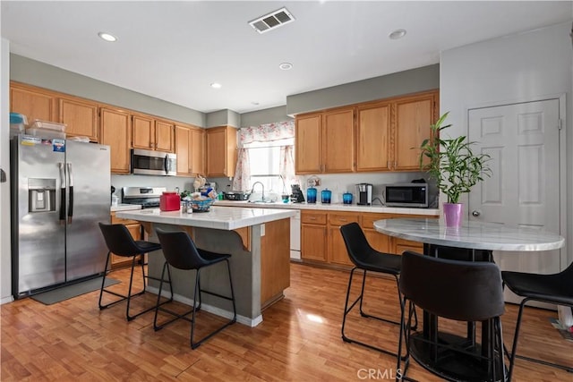 kitchen with sink, stainless steel appliances, light hardwood / wood-style flooring, a breakfast bar, and a kitchen island