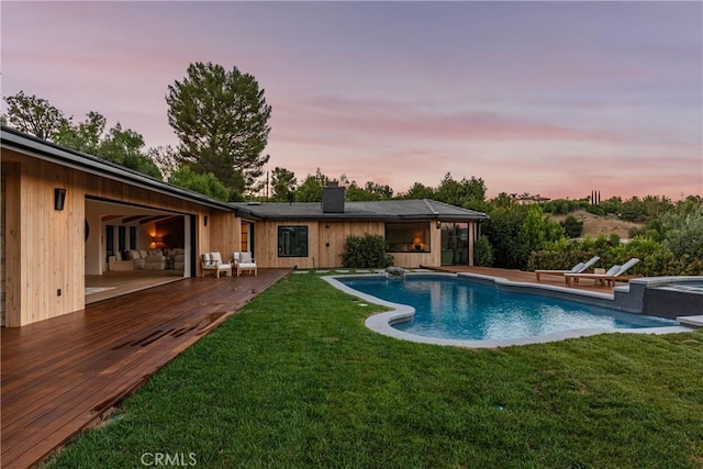 pool at dusk with a wooden deck, an in ground hot tub, and a yard