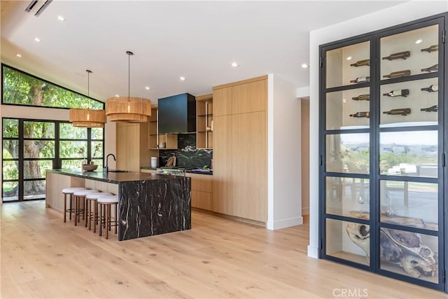 kitchen with dark stone counters, sink, decorative light fixtures, light hardwood / wood-style floors, and an island with sink