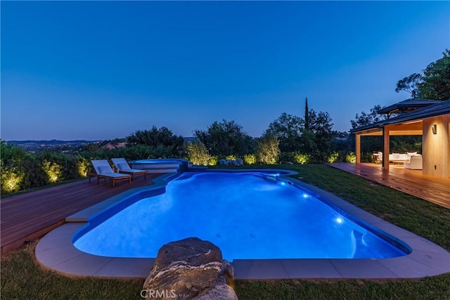 pool at dusk with a wooden deck and an in ground hot tub