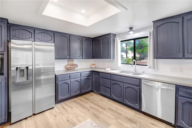 kitchen with a raised ceiling, sink, light hardwood / wood-style flooring, blue cabinetry, and appliances with stainless steel finishes