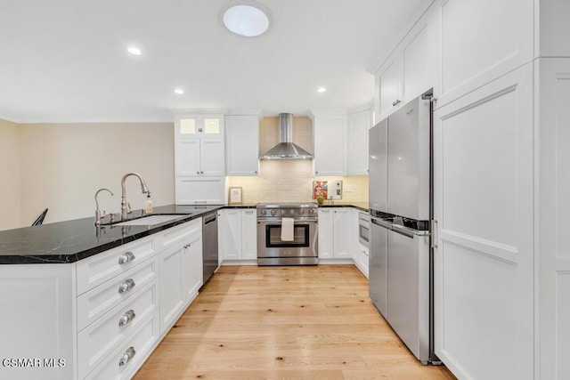 kitchen with dark stone counters, wall chimney exhaust hood, stainless steel appliances, sink, and white cabinetry