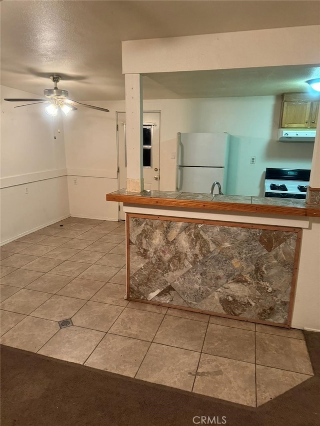 kitchen with light tile patterned floors, under cabinet range hood, stove, a sink, and freestanding refrigerator