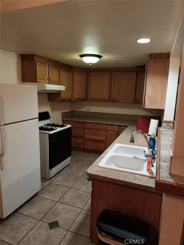 24144 Joshua Ave, Boron, CA 93516 - kitchen with light tile patterned floors, white appliances, under cabinet range hood, a sink, and brown cabinets
