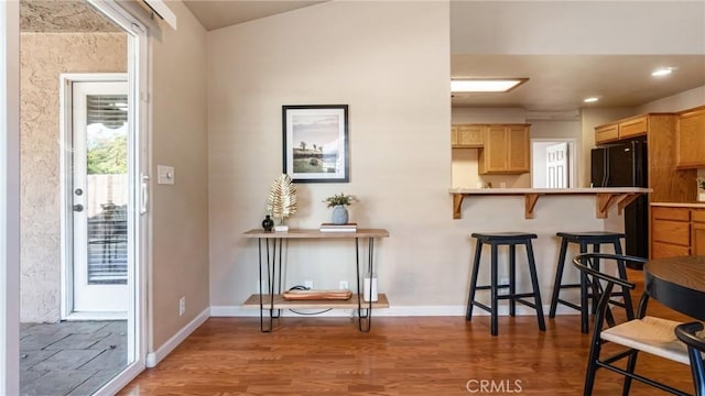 kitchen featuring hardwood / wood-style floors, light brown cabinetry, black fridge, kitchen peninsula, and a breakfast bar area