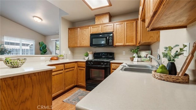 kitchen featuring vaulted ceiling, black appliances, kitchen peninsula, sink, and light hardwood / wood-style flooring