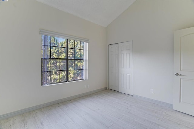 unfurnished bedroom with high vaulted ceiling, light hardwood / wood-style flooring, and a closet