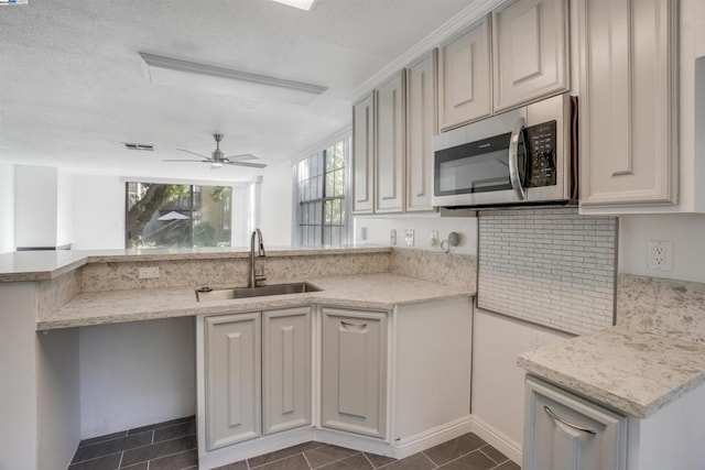 kitchen with backsplash, dark tile patterned flooring, sink, ceiling fan, and light stone countertops