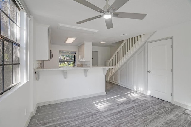 kitchen with a breakfast bar, kitchen peninsula, ceiling fan, light wood-type flooring, and white cabinetry