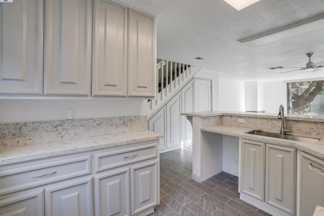 kitchen with ceiling fan, sink, and light stone countertops