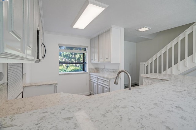 kitchen with kitchen peninsula, white cabinetry, crown molding, and light stone counters