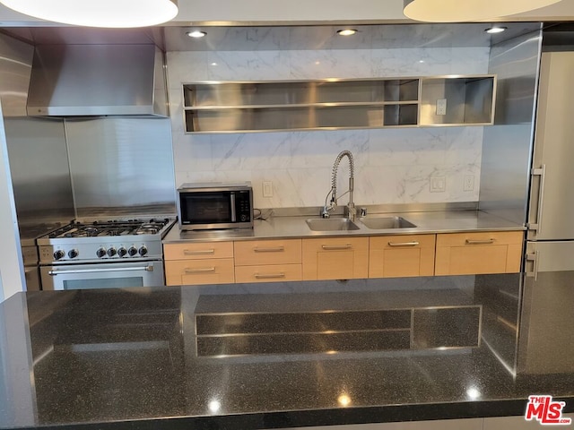 kitchen with appliances with stainless steel finishes, light brown cabinetry, sink, and wall chimney range hood